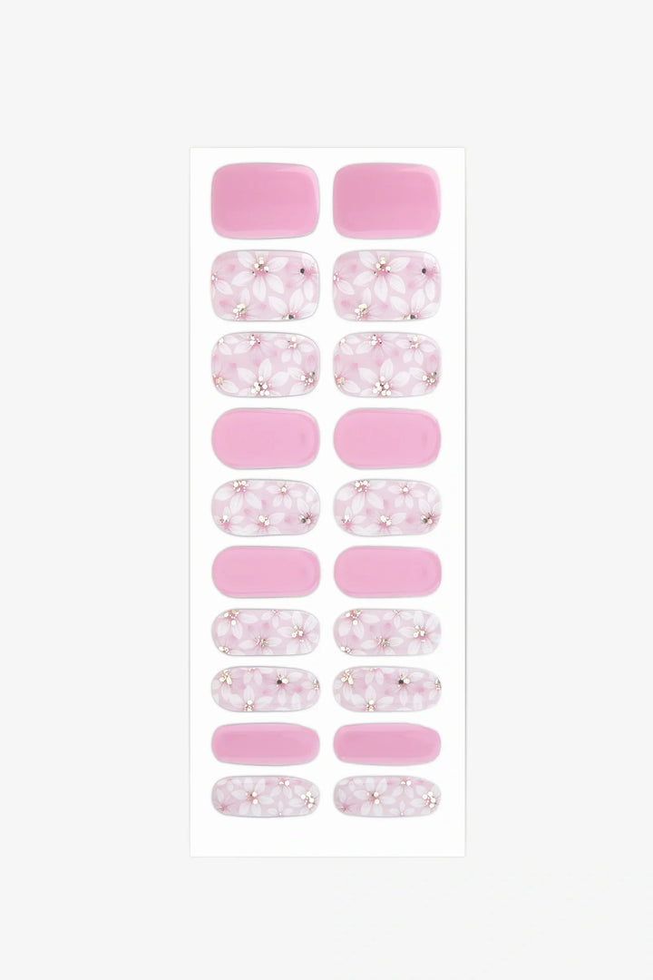 Sheet of semi-cured gel nail wraps in blush pink and white floral designs with golden accents and a glossy finish.