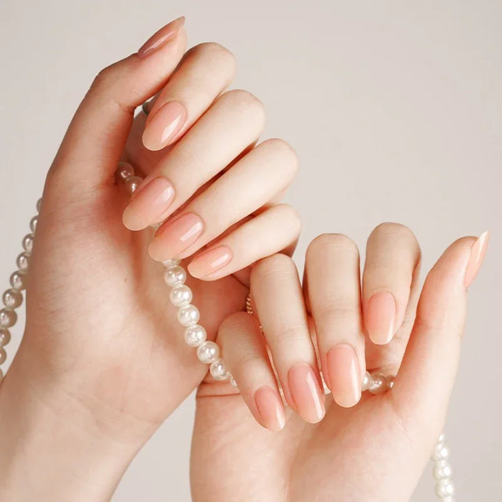 Semi-cured gel nail wraps in sheer blush pink with a soft translucence and glossy high-shine finish, shown on fair skin holding a pearl necklace.