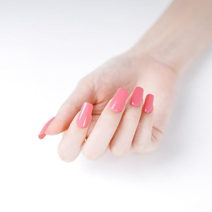 Bright coral glossy gel nails on a light-skinned hand against a white background.