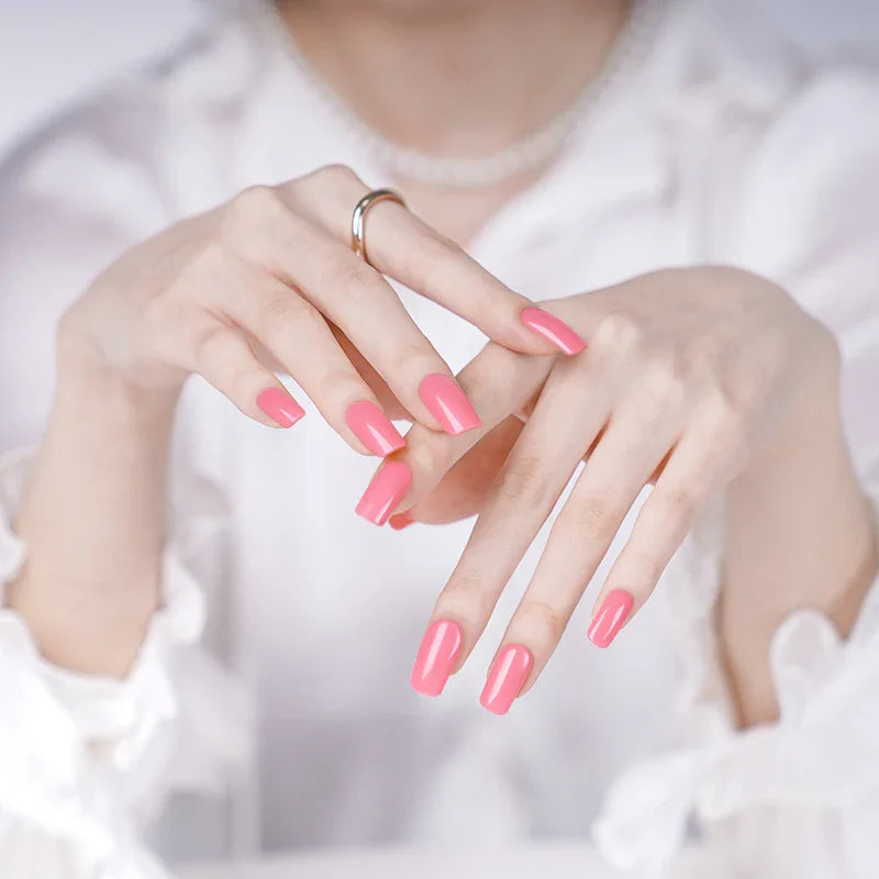 Bright coral gel nail wraps on light-skinned hands with a glossy finish, fingers elegantly posed against a white blouse.