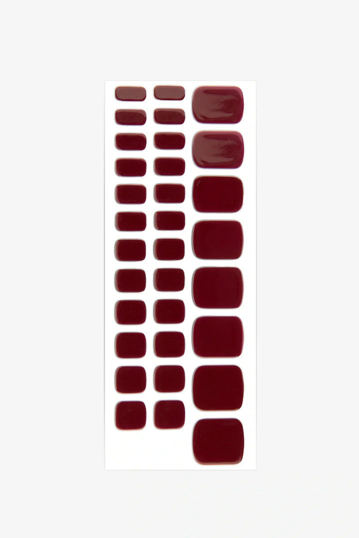 Sheet of burgundy red gel toenail stickers in assorted sizes on a white backing.