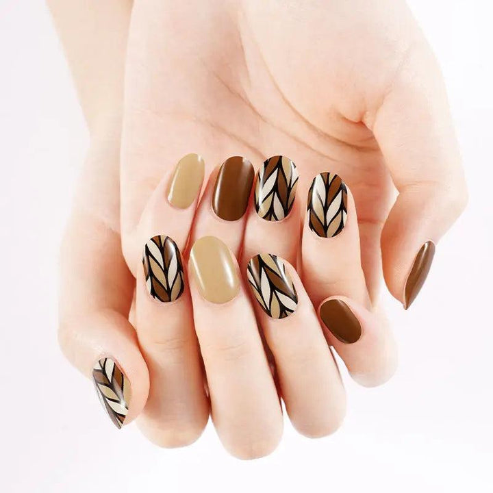 Caramel and nude gel nail wraps with black and beige geometric leaf accents, glossy finish on light skin tone under bright studio light.