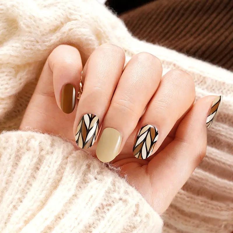 Caramel nude gel nail wraps with glossy black geometric accents on light skin tone, styled with beige knit sleeve in warm indoor light.