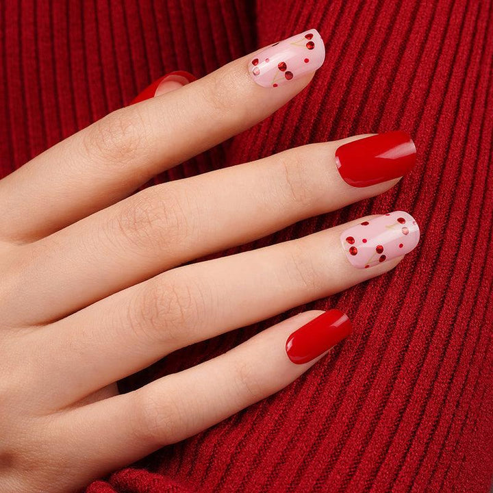 Cherry red and soft pink gel nail wraps with glossy finish and tiny red dot accents on light skin tone, styled against textured red knit fabric.