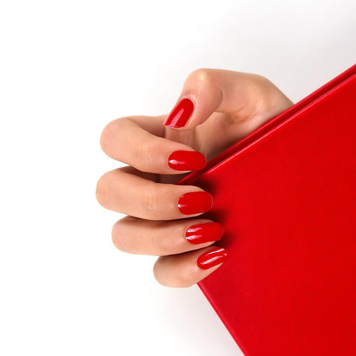 Light-skinned hand with crimson red gel nail wraps in a high-gloss finish against a white background.