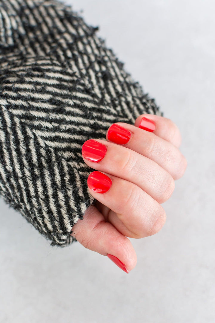 Light-skinned hand with vibrant red glossy gel nails styled with a black and white textured sweater.