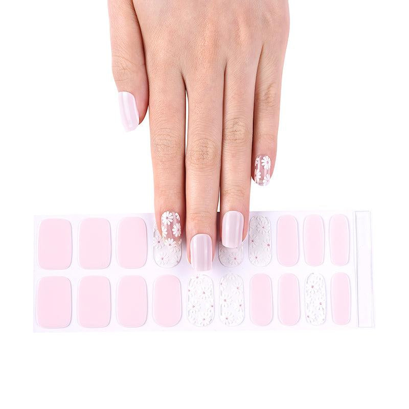 Sheet of baby pink gel nail strips with sheer white daisy designs and glossy finish, shown under bright light.
