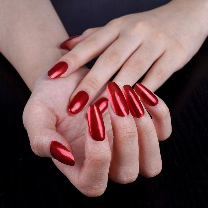 Metallic red gel nail wraps with high-gloss finish and subtle sheer shine on light skin tone, photographed against dark background.