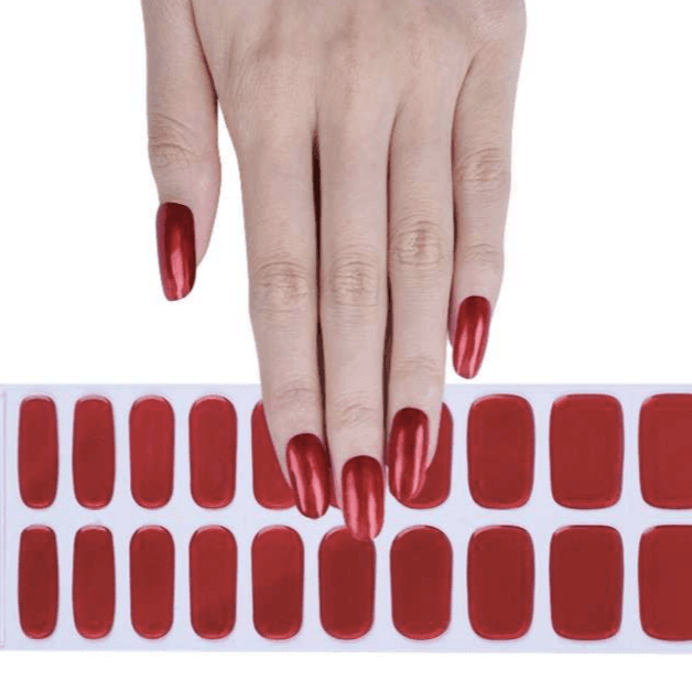 Sheet of metallic red gel nail strips with glossy finish and subtle translucent tone on light skin tone under bright light.