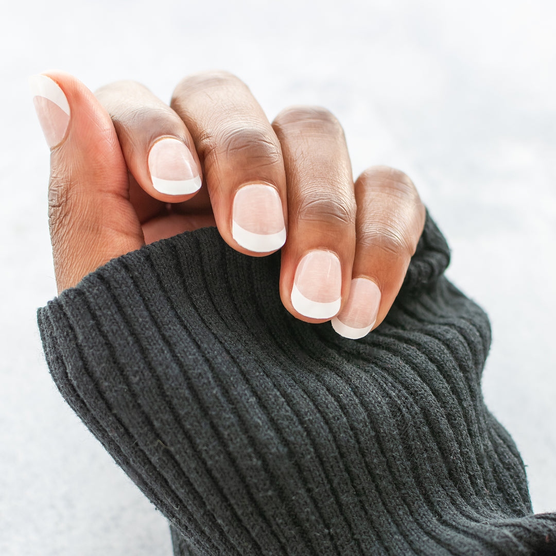 Close-up of a hand wearing semi-cured gel nail stickers displaying built-in French-tip nail art.
