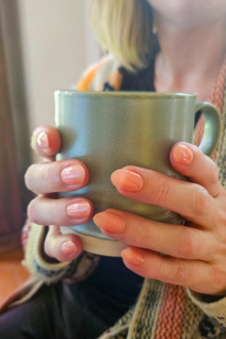 Hands with glossy peach gel nail wraps on cool-toned skin, showing natural translucent finish.