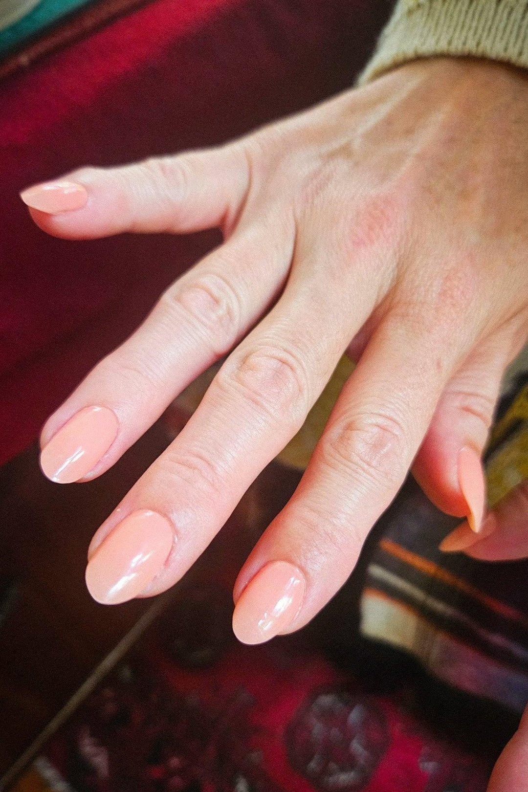 Hand with peach gel nail wraps reflecting soft warm light, showing semi-sheer glossy finish on light skin tone.