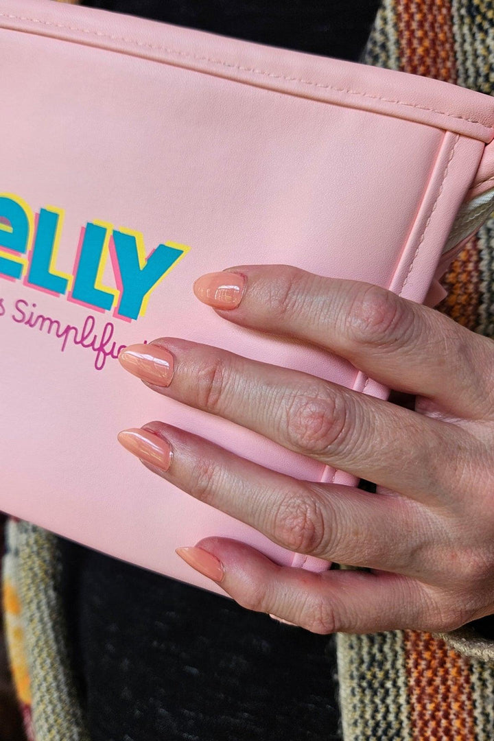 Close-up of hands wearing soft peach gel nail wraps holding a pink pouch, highlighting glossy sheen.