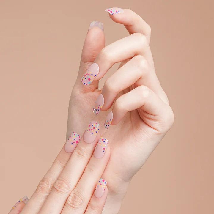 Nude gel nail wraps with multicolor dot design on light skin tone, soft glossy finish in natural daylight.