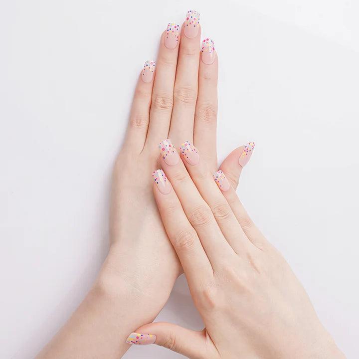 Warm nude gel nail wraps with glossy finish and rainbow polka dots on light skin tone, photographed in bright light.