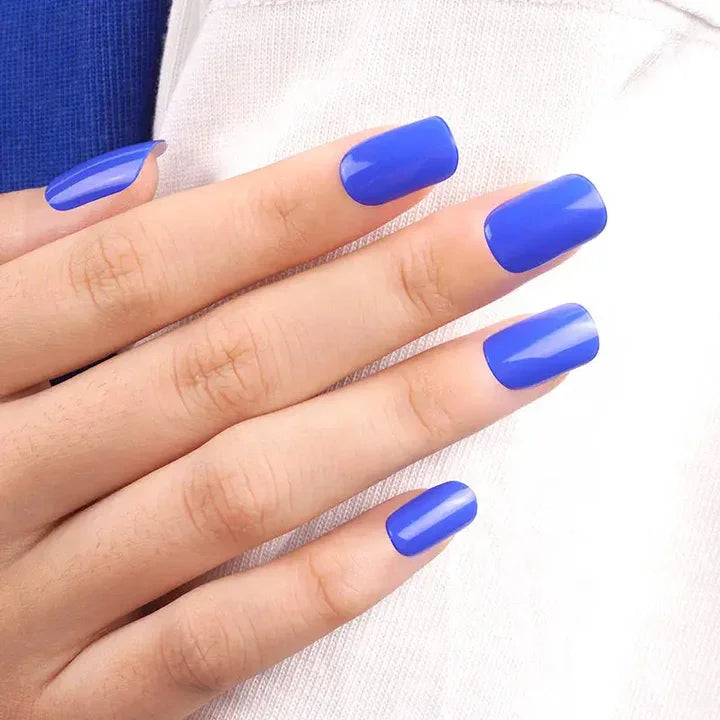 Royal blue semi-cured gel nail wraps with smooth high-gloss surface on light skin tone, photographed in natural light against white fabric.
