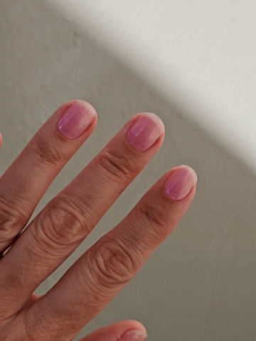 Animated close-up of semi-cured gel nail wraps in translucent pink showing moving cat-eye shimmer in sunlight on medium skin tone.