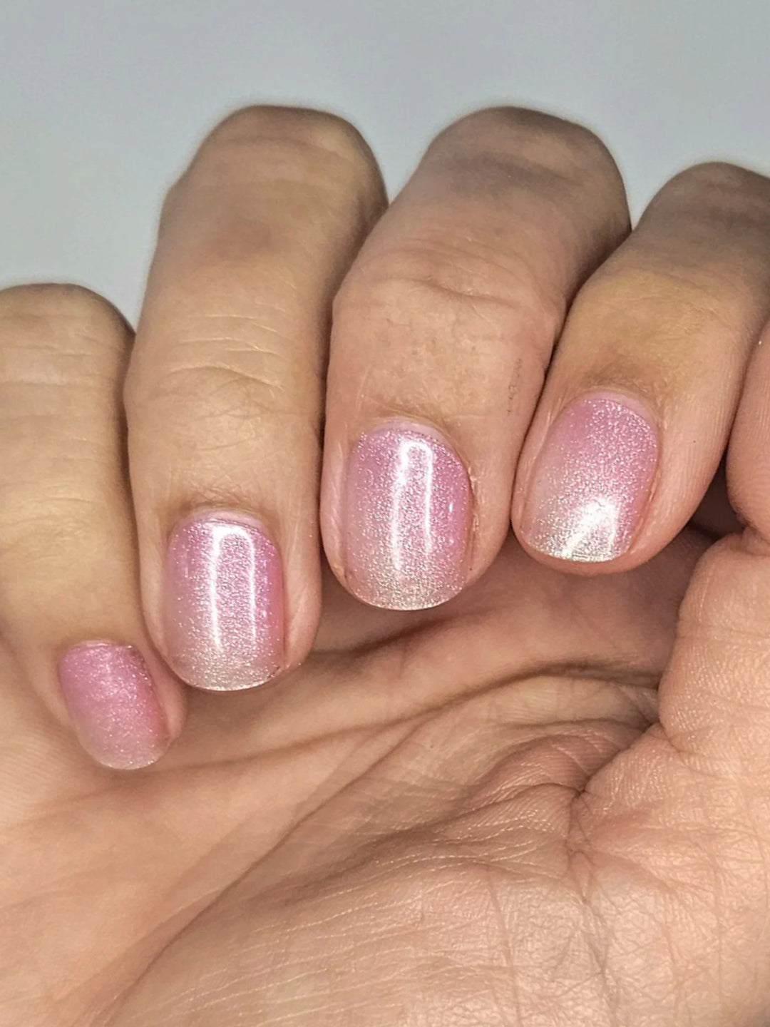 Semi-cured gel nail wraps in translucent pink with soft shimmer and glossy finish, shown on medium-deep skin under diffused light.