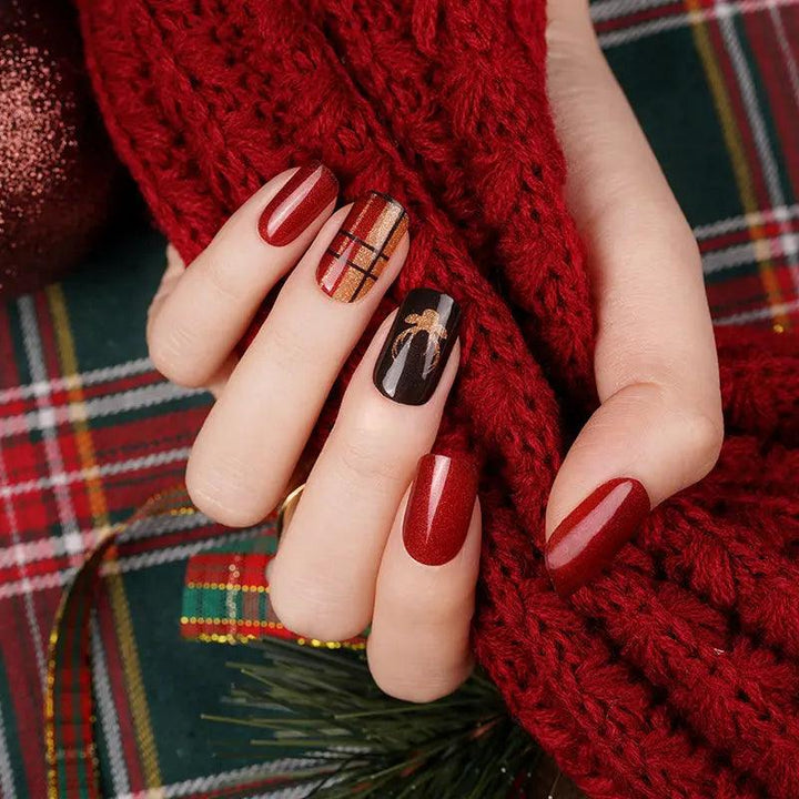 Red shimmer gel nail wraps with gold and black plaid accents on light skin tone, styled with cozy red knit texture.