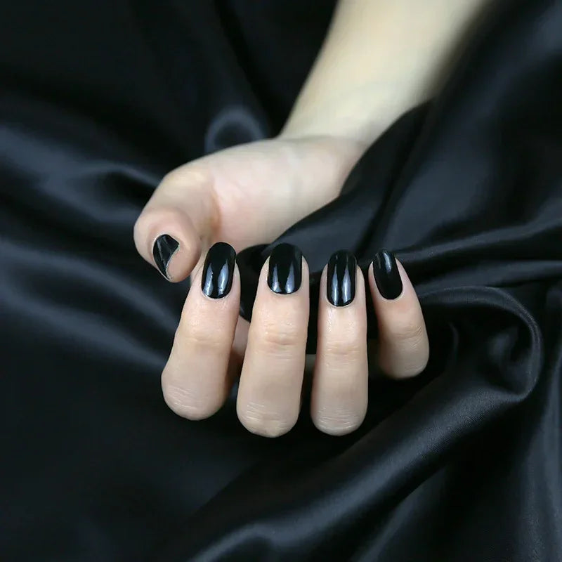 Semi-cured gel nail wraps in deep gloss black with a sleek mirror finish, shown on fair skin against black satin fabric.