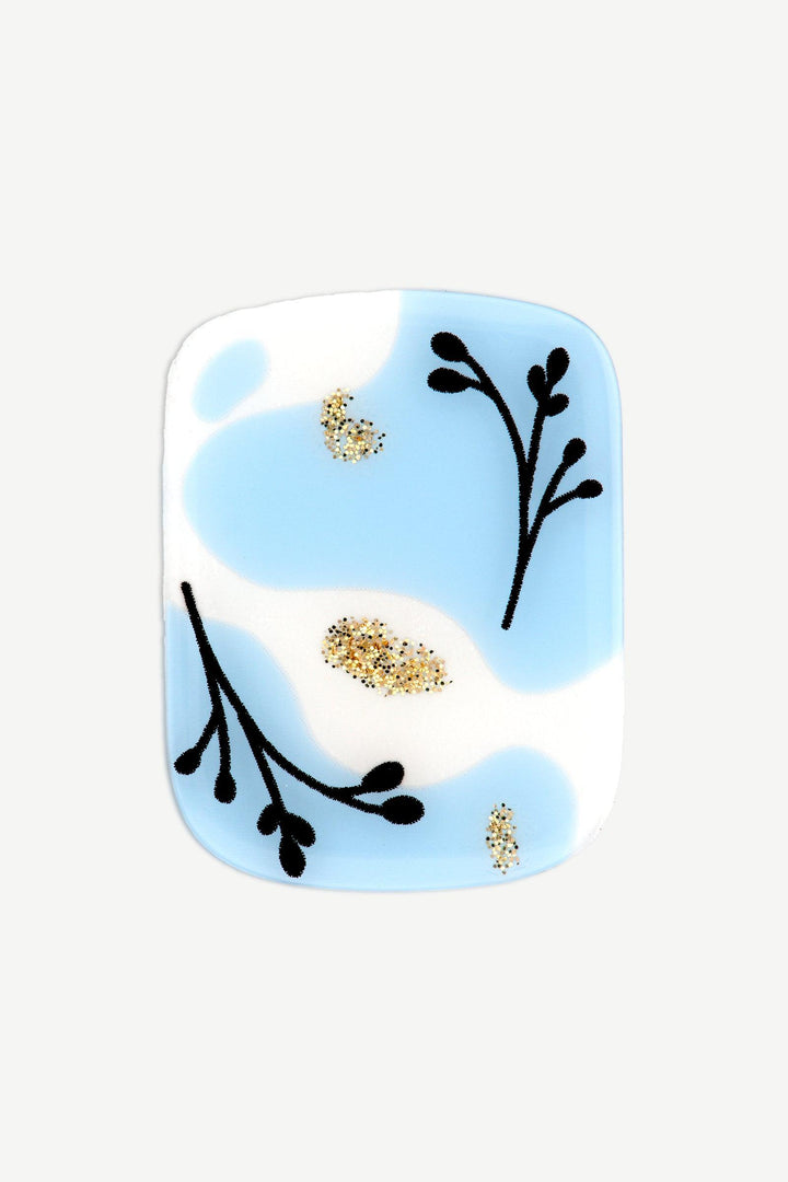 Macro image of a gold and blue gel nail sticker with transparent sections, black botanical lines, and shimmering gold glitter accents.