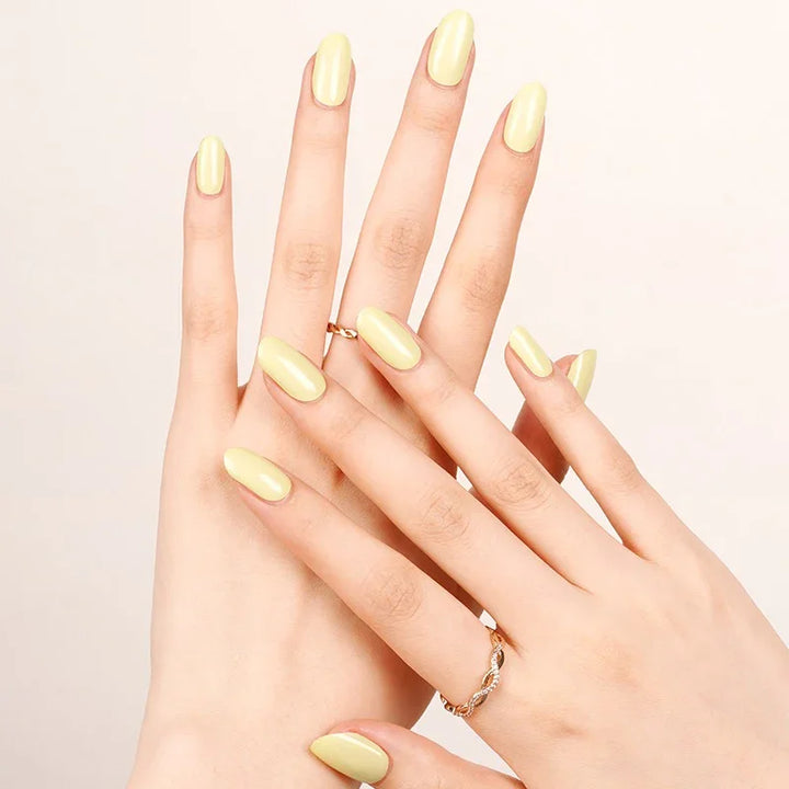 Semi-cured gel nail wraps in pastel yellow with a creamy gloss finish, shown on fair skin wearing delicate gold rings.
