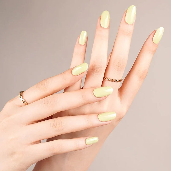 Semi-cured gel nail wraps in pale buttery yellow with a glossy shine, shown on light skin with gold jewelry under warm lighting.