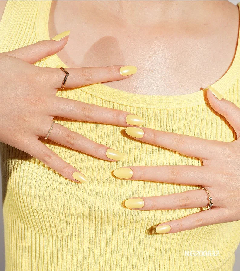 Semi-cured gel nail wraps in bright butter yellow with a subtle shimmer and glossy finish, shown on fair skin wearing gold rings and a yellow ribbed top.