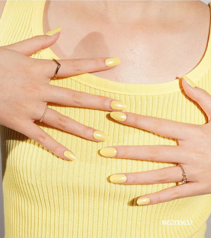 Semi-cured gel nail wraps in bright butter yellow with a subtle shimmer and glossy finish, shown on fair skin wearing gold rings and a yellow ribbed top.