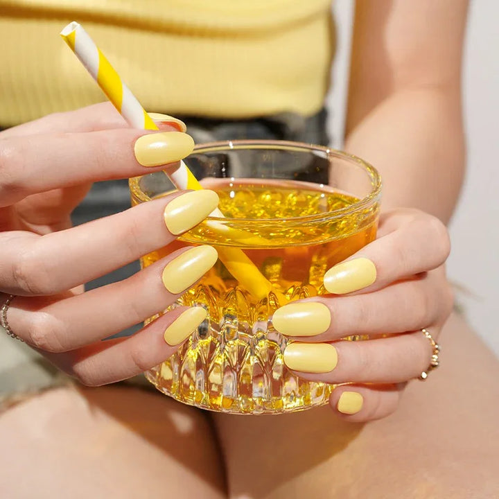 Semi-cured gel nail wraps in sunny pastel yellow with a light shimmer, shown on light-medium skin wearing gold jewelry in warm natural light.