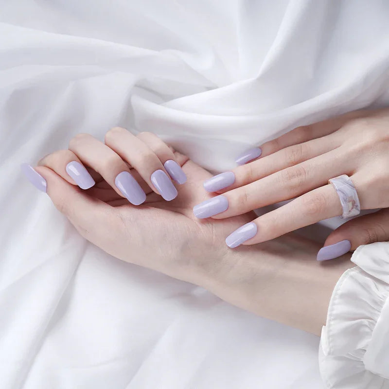 Lilac purple gel nail wraps with cool undertone and glossy finish on light skin tone, styled with a marble ring and white sleeves.