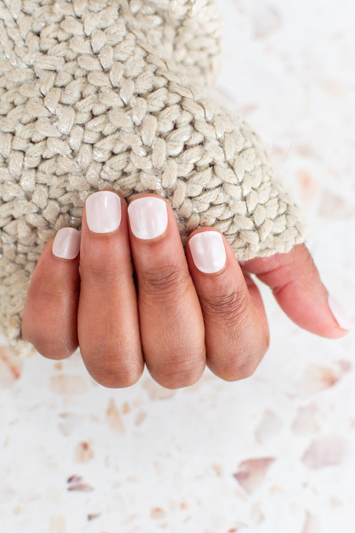 Close-up of soft beige semi-cured gel nail strips on medium skin tone, paired with a chunky knitted cream sweater under natural lighting.