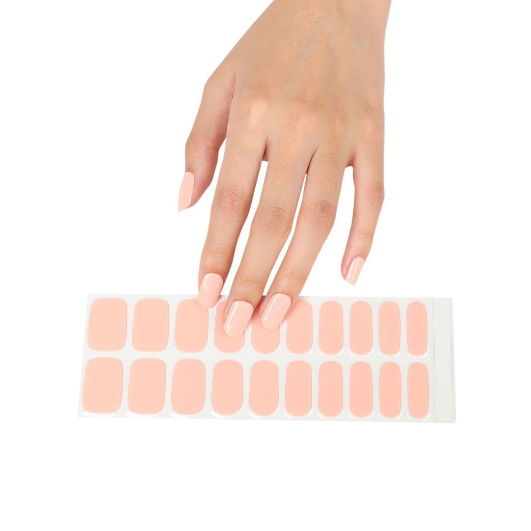 Light-skinned hand with a full strip of nude peach glossy gel nail stickers.