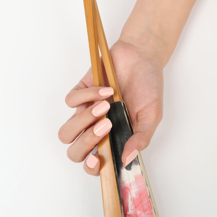 Light-skinned hand with nude peach glossy gel nail wraps, showing a natural, soft-toned manicure.
