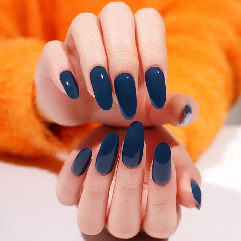 Cool-toned navy blue gel nail wraps with mirror-like gloss on light skin tone, styled with textured orange knit clothing.