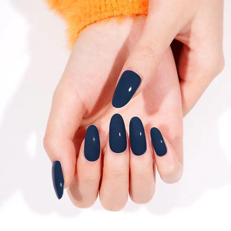 Rich navy blue glossy gel nail wraps on light skin tone with bright orange sweater in soft daylight.