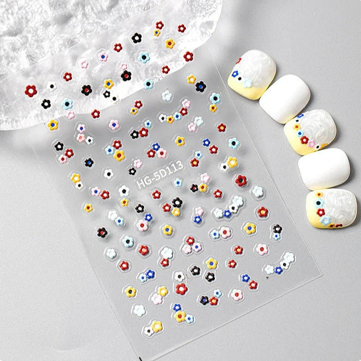 Colorful nail art stickers on a clear sheet with white nail decorations.