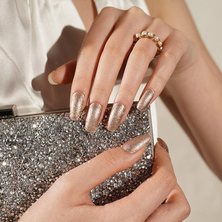 Rose gold shimmer gel nail wraps with sheer champagne tone and high-gloss finish on light skin tone, styled with rings and silver clutch