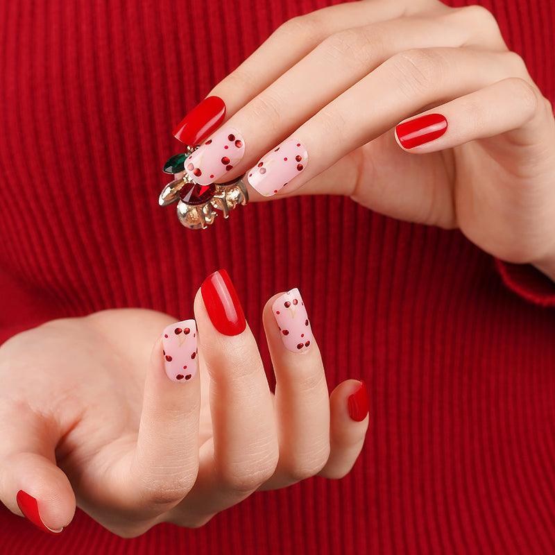 Bright red and semi-cured gel nail strips with metallic cherries and glossy finish on light skin tone styled with a red sweater.