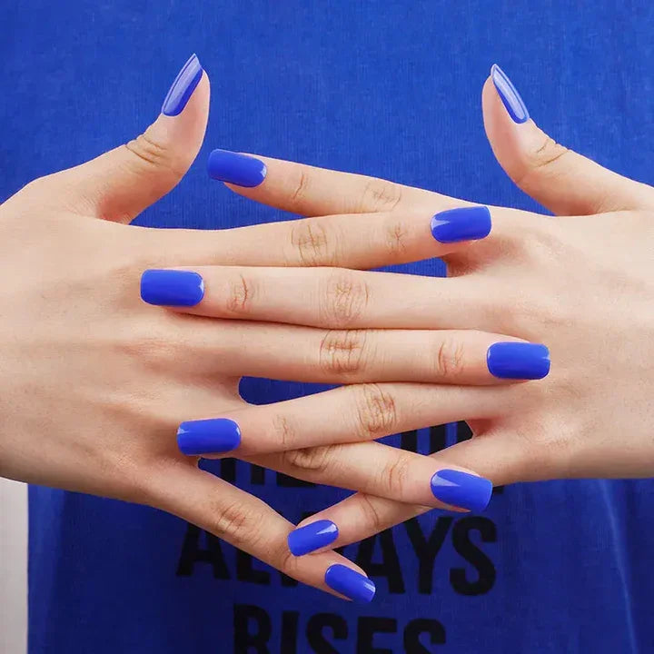 Royal blue stick-on gel nails with bold glossy finish on light skin tone, styled with blue clothing under bright studio lighting.