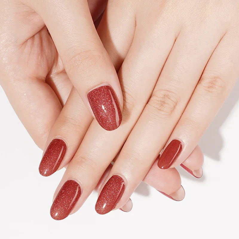 Semi-cured gel nail wraps in warm brick-red with fine magnetic shimmer and a glossy cat-eye finish, shown on light skin with neatly shaped nails.