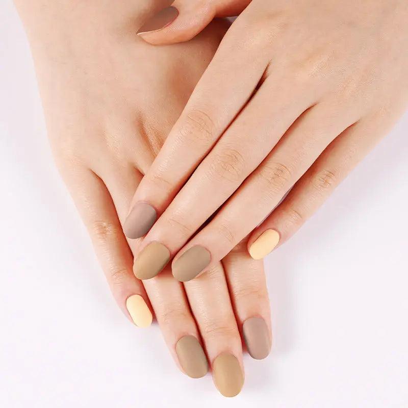 Warm neutral matte gel nail wraps in tan and cream gradient shades on light skin tone, soft daylight setting.