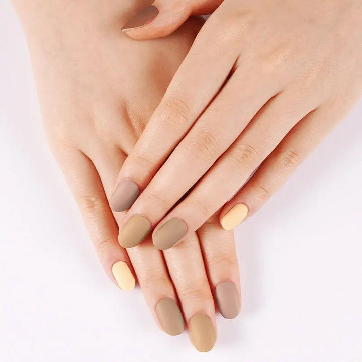 Warm neutral matte gel nail wraps in tan and cream gradient shades on light skin tone, soft daylight setting.