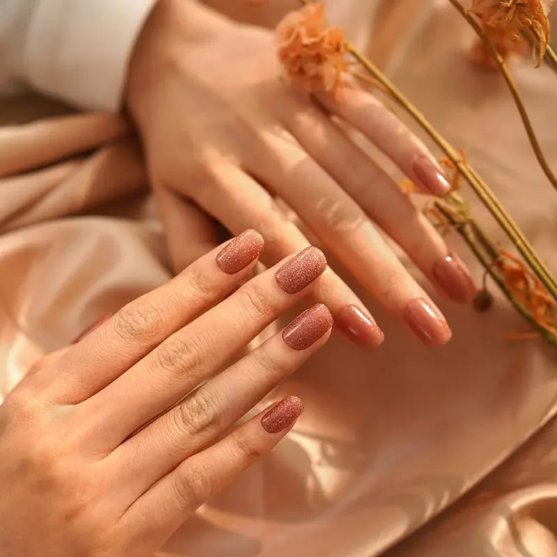Semi-cured gel nail wraps in shimmering gold with a glossy cat-eye glow, shown on light skin in soft amber lighting.