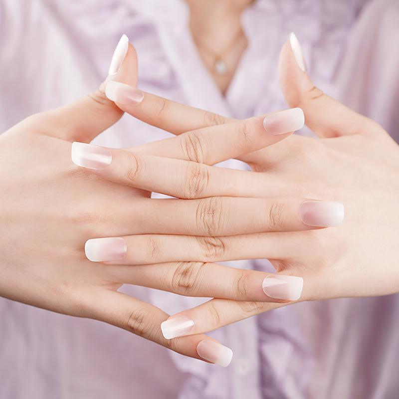 Hands wearing sheer nude ombré gel nail wraps with glossy finish, styled against soft pink clothing.