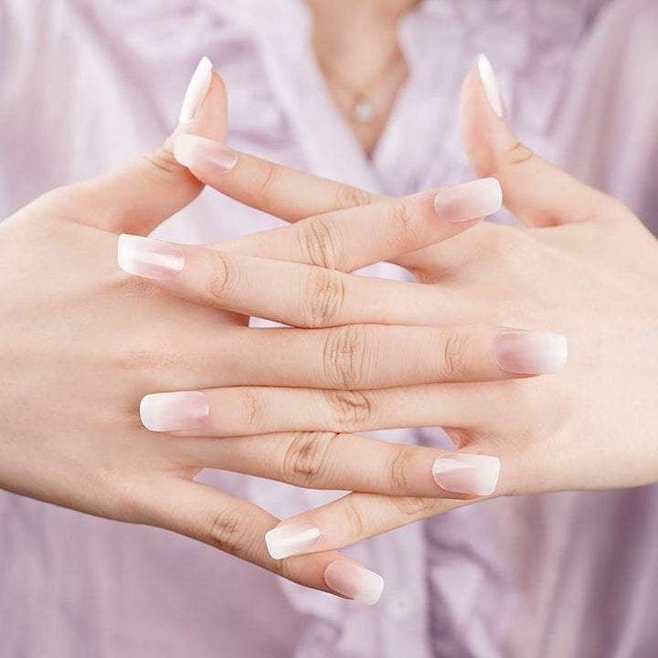 Hands wearing sheer nude ombré gel nail wraps with glossy finish, styled against soft pink clothing.