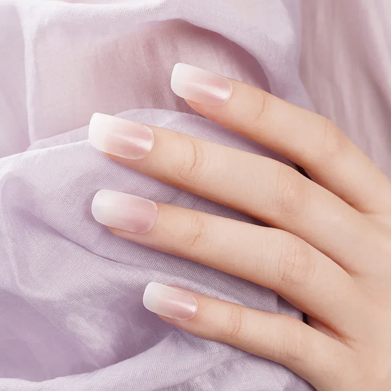 Semi-transparent nude ombré gel nail wraps with glossy finish on light skin tone, photographed against soft lilac fabric.