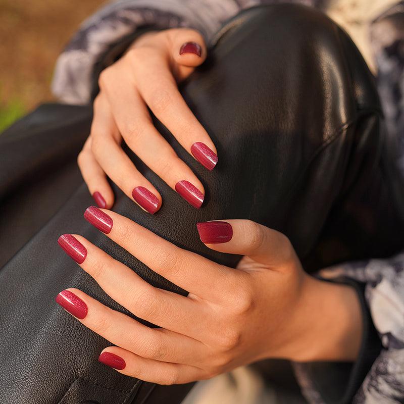Shimmering magenta gel nail wraps with glossy finish on light skin tone, styled with black leather.