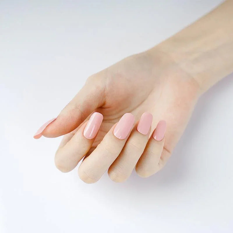 Muted peach stick-on gel nails with subtle coral tone and glossy finish on light skin tone under soft lighting.