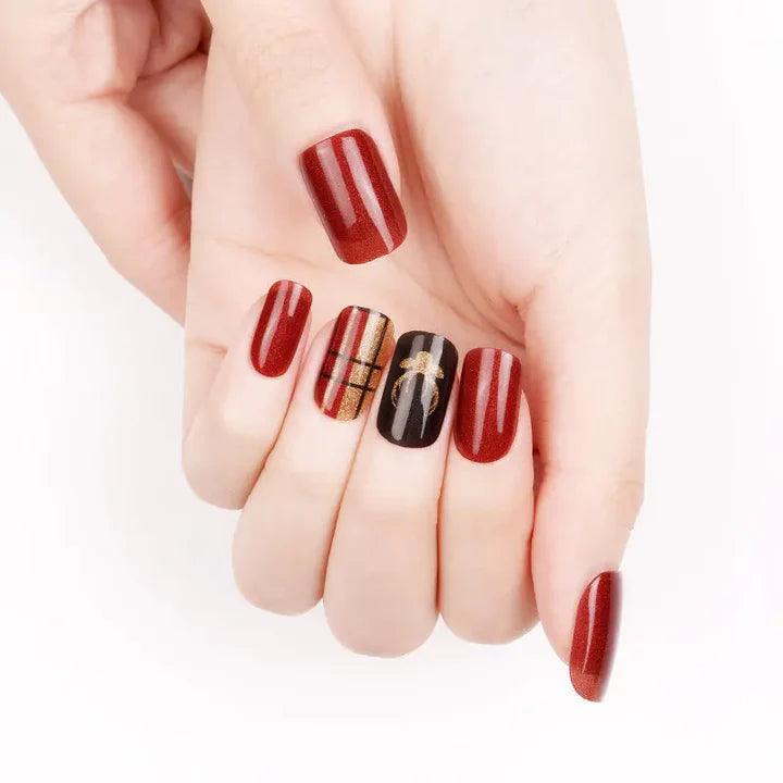 Deep red gel nail wraps with gold plaid and black stag accent nails on light skin tone, glossy finish and festive shimmer.